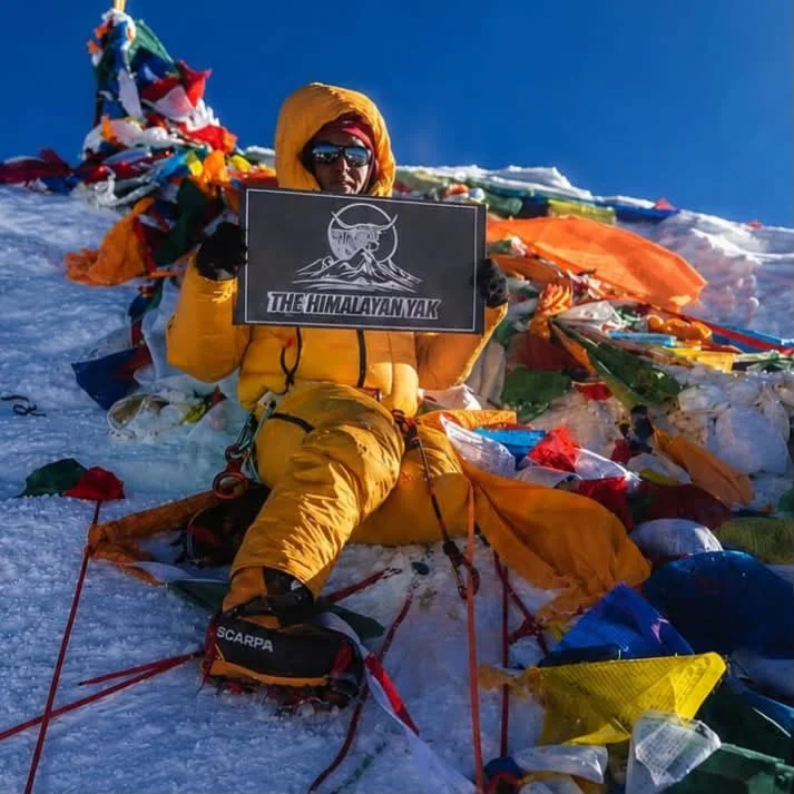 Mr. Prmba Nuru Sherpa in mountaineering gear holding The Himalayan Yak sign on Mount Everest
